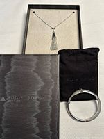 Jewelry set with necklace displayed in box and hinged bracelet with black pouch and box visible.