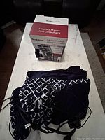 One photo showing a boxed Brookstone Heated Throw next to a folded black, white, and gray plaid heated throw with attached remote controller cords.