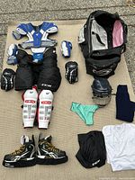 Full set of men's hockey gear items including pads, skates, helmet, bag, and apparel arranged on floor