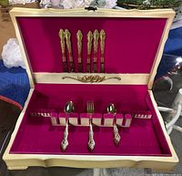 Full open storage box showing three types of flatware arranged inside and in the lid set against a pink background.