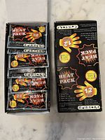 Open box showing multiple individually wrapped ultra thin hand warmer packets inside black and orange packaging.