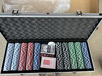 Open poker case showing multicolored poker chips, playing cards, and dealer button arranged in foam compartments.