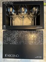Two black boxes containing six Krosno wine glasses each, total of 12 glasses, unopened in original packaging, labeled Made in Poland, dishwasher safe.