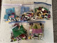 Five transparent Ziploc bags containing mixed LEGO pieces viewed from above on a wooden surface.