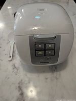 Closed Panasonic rice cooker with control panel showing cooking mode buttons and power indicators, and serving paddle beside it.