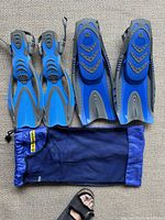 Two pairs of blue and gray snorkeling fins laid flat with a blue mesh carry bag below, showing overall condition and colors