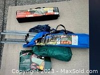 Three camping items: blue canopy tent in bag, green air mattress in bag, and packaged Coleman item, all displayed on floor.