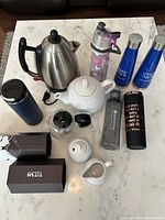 Full view of tea and thermos set showing all items on marble surface, including kettle, teapot, creamer, sugar container, bottles, and thermos.