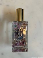 Clear rectangular perfume bottle with gold cap, decorative floral artwork label and gold text showing brand 'Tokyomilk' and '49'.