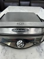 Closed waffle maker showing the Calphalon brand logo and temperature control dial on the front panel.