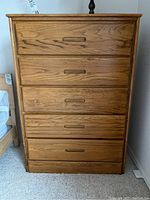 Front view of the tall oak dresser showing five drawers with inset wooden handles.