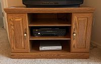 Front view of the pressed wood TV stand showing cabinet doors, open shelves, Panasonic VHS player, and Magnavox DVD player.