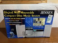 Front view of boxed Jensen Digital Wall Mountable Compact Disc Music System showing product image and key features.