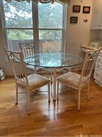 Front view of round glass kitchen table with white metal base and four white metal chairs with cushioned seats. Visible stains on chairs.