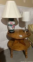 Side table with floral ceramic lamp and metal base lamp on top, view of table's round top surface and lampshades.