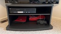 Frontal close-up of TV stand shelving with DVD/VHS player on top shelf and other items below