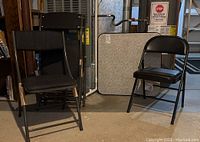 Group photo of multiple black folding chairs arranged near vintage card table area. Includes chairs with different upholstery types under ambient basement lighting.