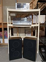 Wide photo of stereo components on a plastic storage rack with visible microphones, receiver, and speakers arranged in basement storage