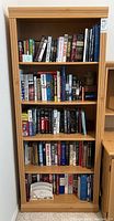 Front view of tall pine wood bookcase filled with books on all four shelves.