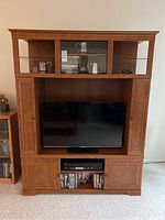 Front view of the wood entertainment unit showing TV, DVD player, DVDs, and shelving.