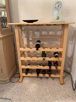 Front view of wood wine rack holding ten wine bottles and six hanging wine glasses with decorative items on top.