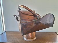 Side profile of the antique copper coal skuttle showing the broad pouring spout, curved top handle, and overall polished copper surface.