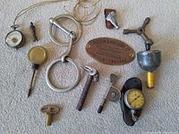 Full collection of antique mechanical and measuring tools laid out on carpet including pressure gauge, key, metal rings, and identification plate.