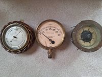Three antique marine instruments laid side by side on a grey surface