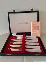 Set of six brand new stainless steel butter knives with mother of pearl handles displayed in original black box with red insert and white satin lid lining with gold branding