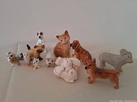 Collection of 11 ceramic animal figurines displayed on a flat surface, including dogs, small owls, a ram, and piglets, arranged in two rows.