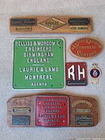 Photo showing multiple brass and metal engine plates arranged on a flat surface with some mounted on wooden boards.