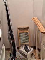 Hoover Linx cordless upright vacuum, antique washboard on a plastic step stool, hand broom, and wooden drying rack in corner