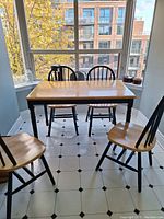 Full view of rectangular kitchen table with four round back chairs in front of large windows.