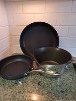 Photo showing two Lagostina non-stick frying pans (10 inch and 8 inch) and one KitchenAid non-stick pot with polished stainless steel exterior and spout, all on kitchen countertop.