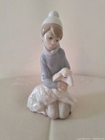 Front angled view of the figurine showing the boy holding a lamb, highlighting delicate facial features and clothing detail.