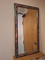 Full view of the rectangular mirror reflecting a door, showing the entire floral painted frame with gold trim.