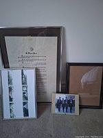 Photo showing four picture frames of various sizes and styles arranged on carpet. Largest frame contains printed text with a double mat, medium frames include one with photo strip art and one empty black frame, smallest frame holds photo of four people walking.