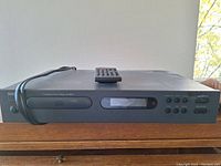 Front view of NAD C 521i CD player showing disc tray, display, control buttons, attached power cable, and remote control on top