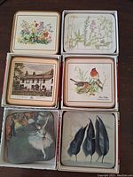 Six sets of Pimpernel coasters, each set in its own white box showing various artwork including floral, botanical, cottage, birds, ballerina, and leaf designs.