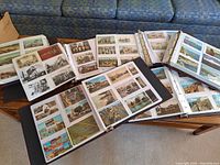 Top-down view of six binders open on coffee table displaying postcards in plastic sleeves