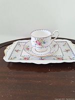 Full view of tea cup, saucer, and rectangular tray displaying matching floral and gold trim patterns.