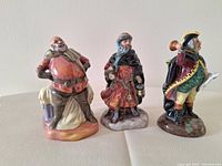 Front view of 3 Royal Doulton figurines - Town Crier, Good King Wenceslas, Falstaff, side by side on cloth surface.