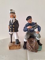 Side-by-side photo showing the wooden carved fisherman figure alongside the ceramic Royal Doulton The Lobster Man figurine