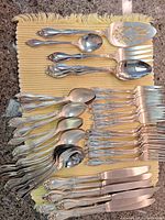 Full layout showing multiple forks, knives, teaspoons, tablespoons, serving spoon, serving fork all matching ornate silver plate pattern.