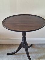 Full view of the solid dark wood side table showing round scalloped top and tripod base with turned pedestal.