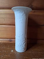 Full front view of matte white porcelain vase with relief floral motifs on wooden background.