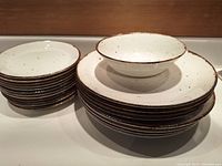 Set of speckled cream ceramic plates and bowl with brown rims showing overall lot contents.