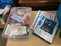 Clear plastic bin filled with various arts and crafts materials including ribbons, beads, and papers, alongside boxed sets of Super Spirograph and Creatology art set