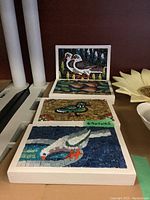 Front view of four bird-themed mosaic plaques arranged in a row showing colorful bird images made with hand-painted tiles in wooden frames.