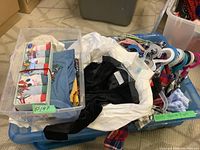 Two plastic totes filled with boys clothing including folded t-shirts, underwear, and shirts on hangers.